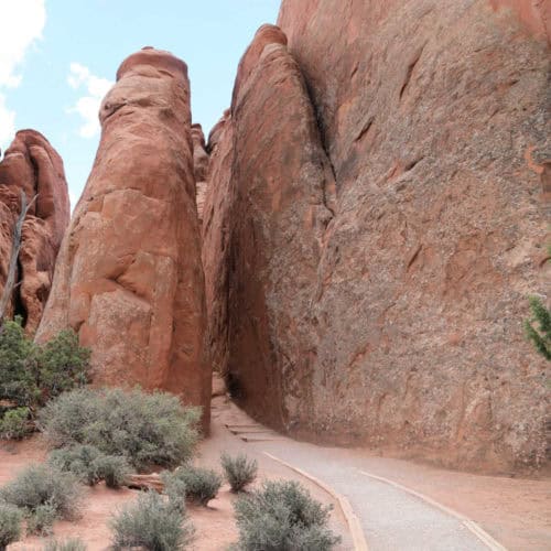 The beginning of Sand Dune Arch Trail in Arches National Park as it enters between a sandstone rock wall and a large sandstone fin (thin rock wall)