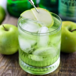 Green Irish Sour Apple Cocktail on a wood board with apples