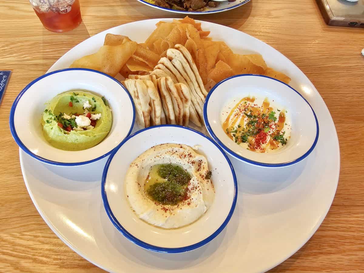 three dips in bowls with pita chips and pita bread