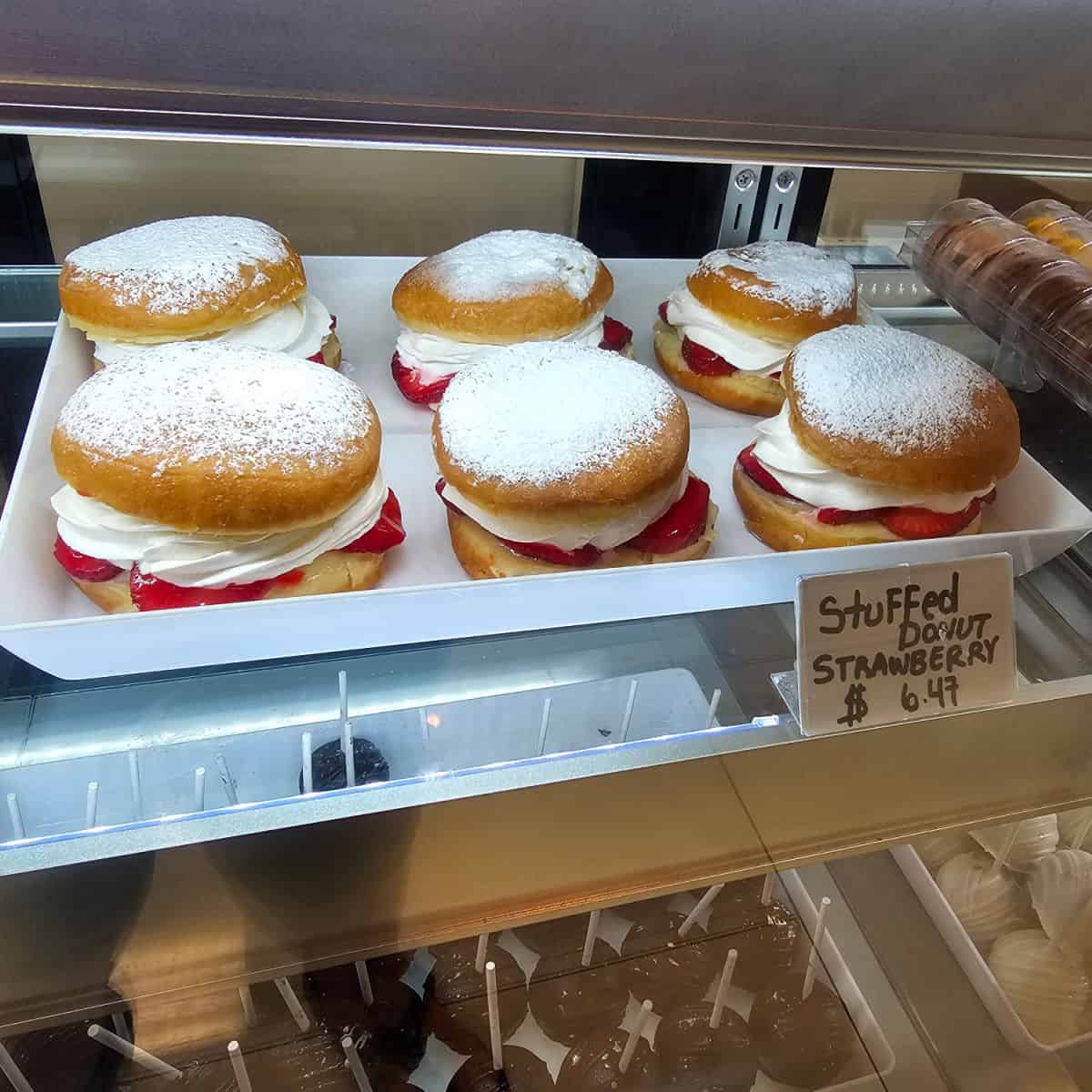 white tray of stuffed strawberry donuts in a bakery case
