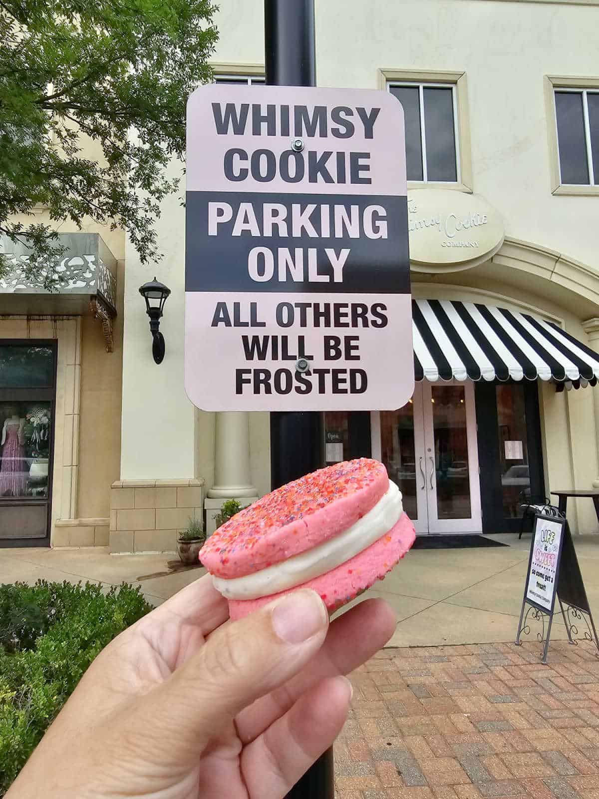 Whimsy Cookie Parking Only all others will be frosted sign above a hand holding a pink sandwich cookie