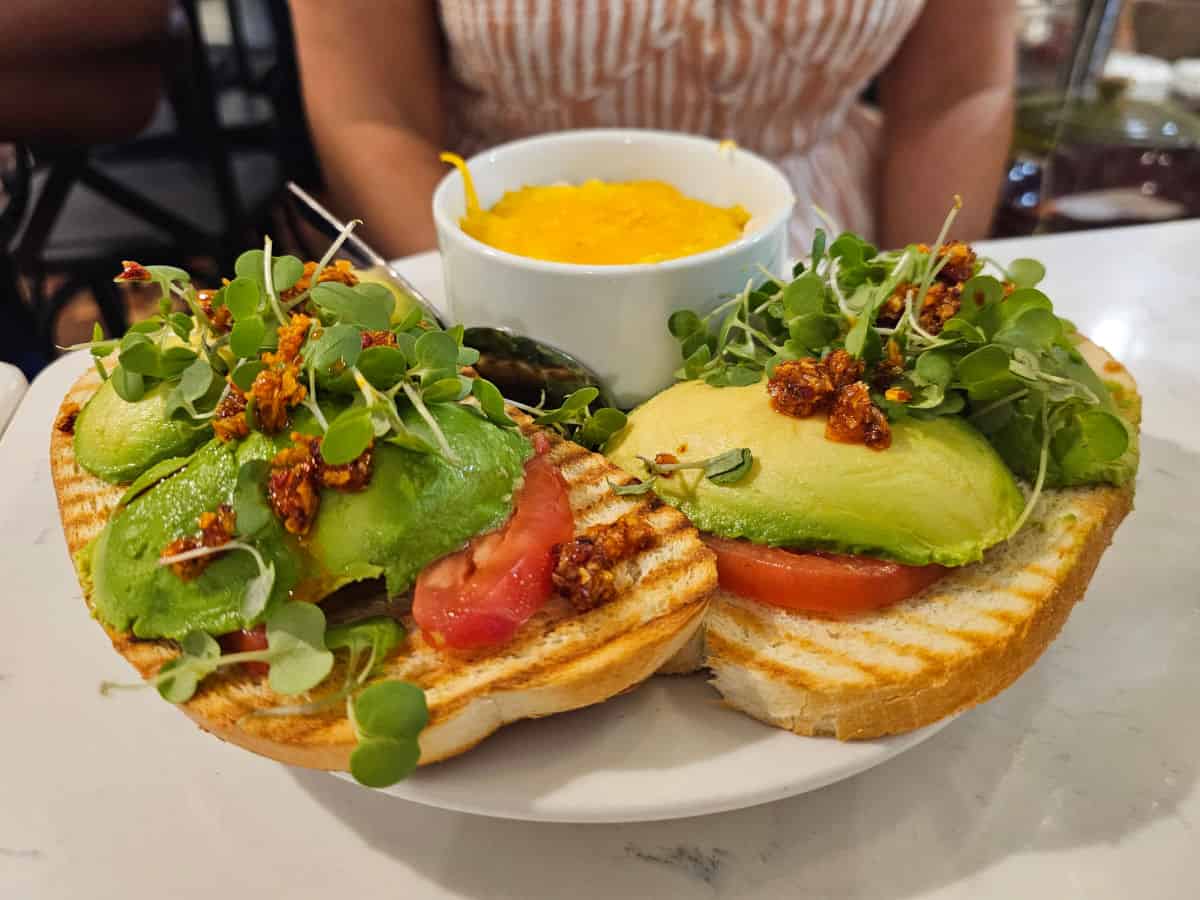 Avocado Toast on a white plate with a bowl of grits