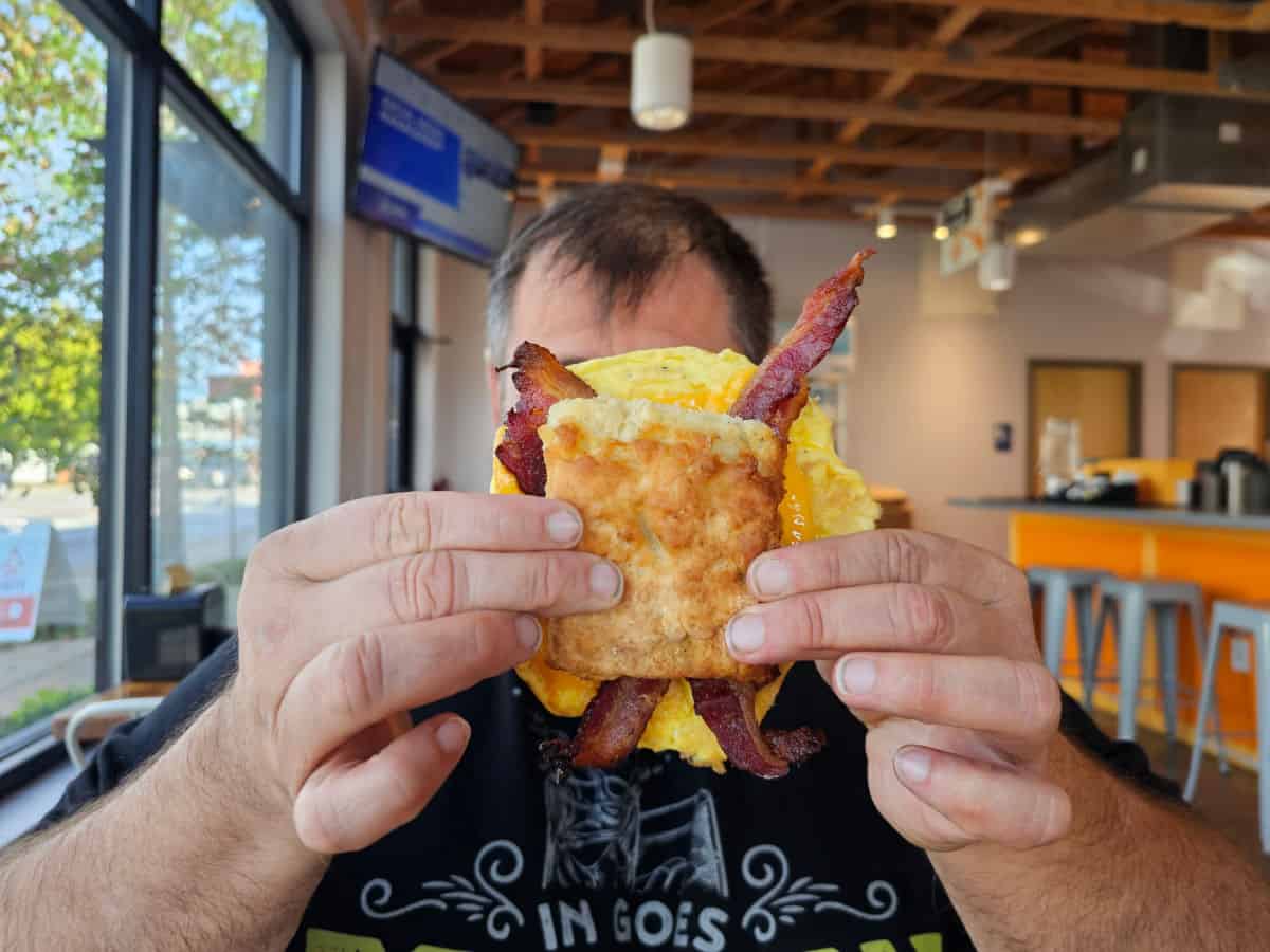 John holding a large bacon egg and cheese biscuit in front of his face