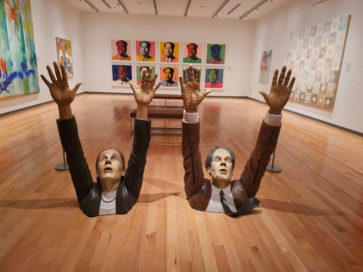 Andy Warhol prints of Chairman Mao on the back wall with sculptures of people holding their arms in the air in front of the prints 