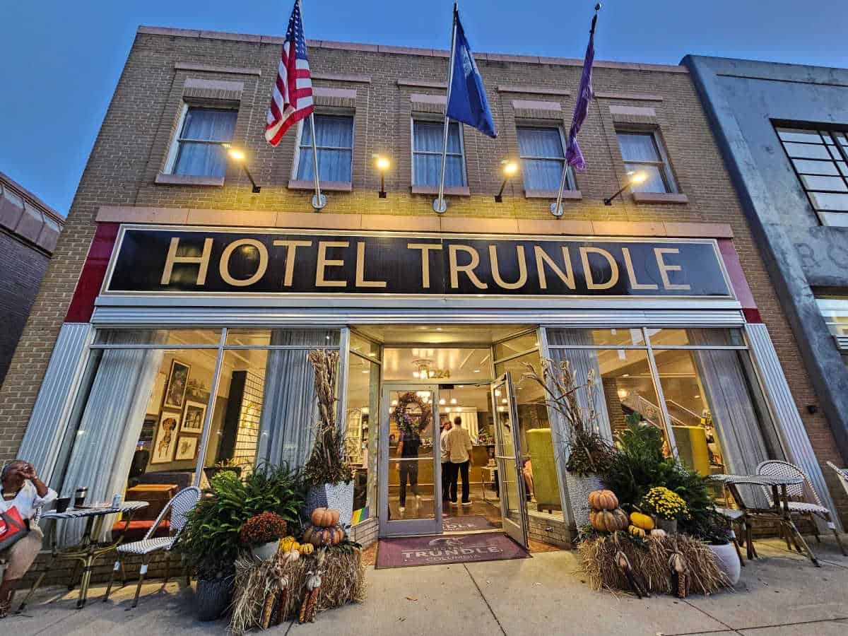 Hotel Trudle sign on a two story brick hotel with flags hanging above the sign, Fall decorations in front of the glass entrance door. 