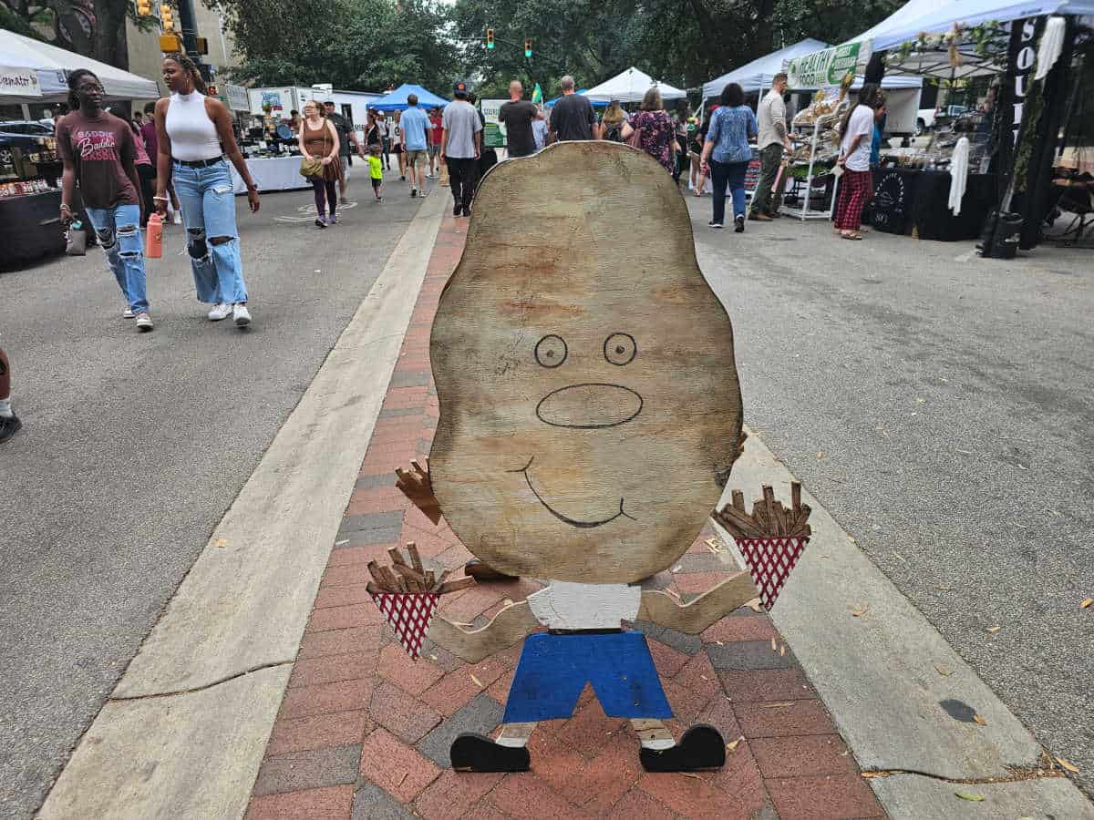 Potato sign holding french fries with market vendors on both side of the street