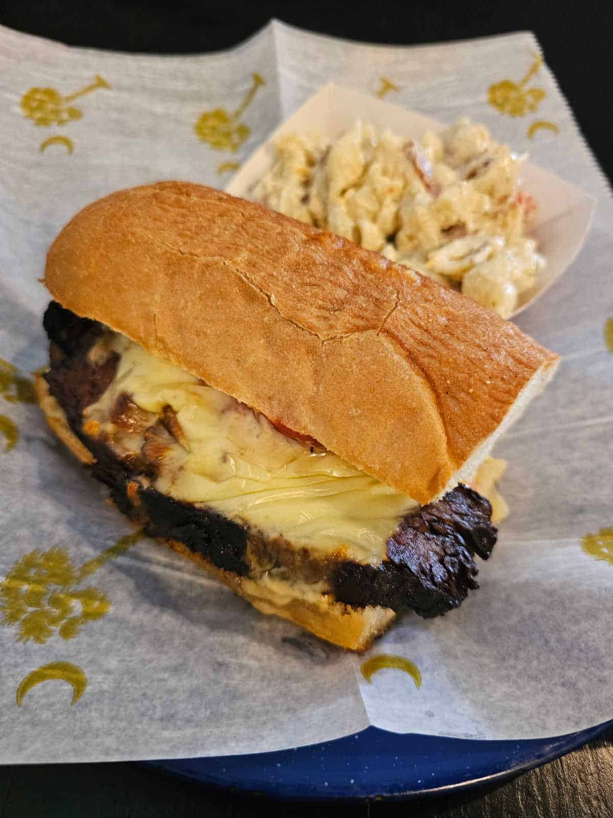 Brisket sandwich on a white paper with a basket of macaroni salad