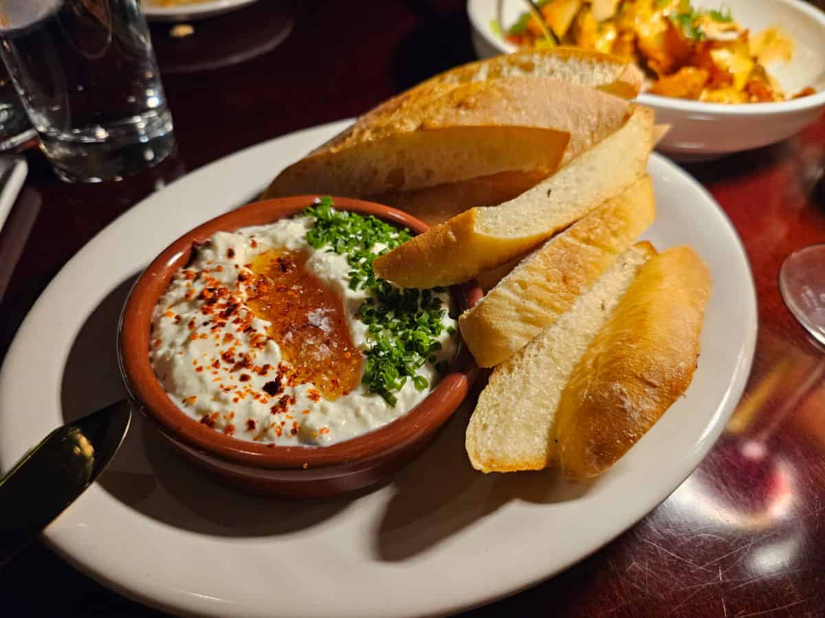 Whipped feta in a bowl next to baguette slices on a white plate