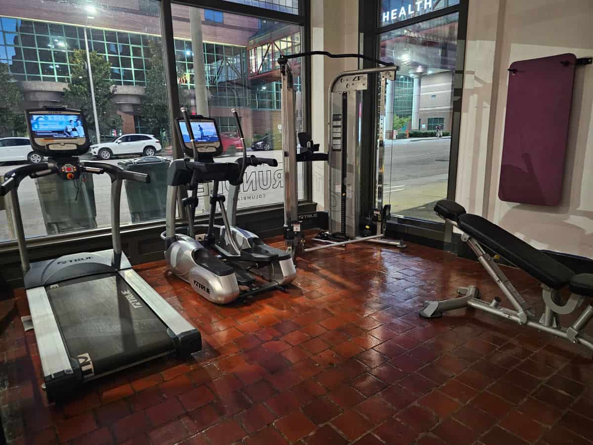 Workout room with treadmill, stair stepper, free weights, yoga mat on the wall and glass windows looking out to the street